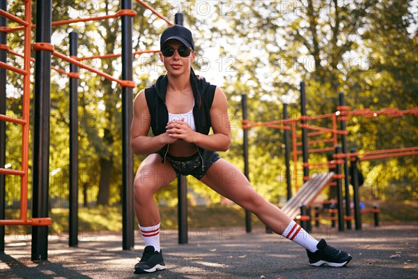 Beautiful young fitness girl is warming up at the stadium before training. Attractive slender brunette in a tracksuit