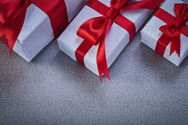 Boxed gifts with tied red ribbons on grey surface directly above holidays concept