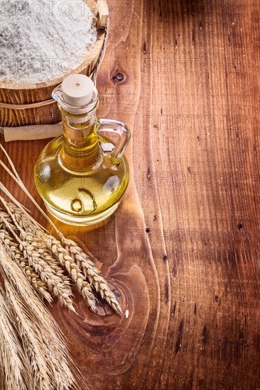 Bottle with oil bucket of flour wheat ears on vintage wooden board with copyspace food and drink concept