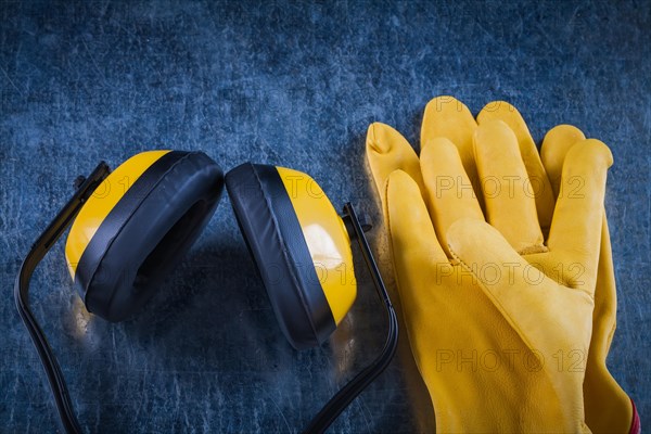 Protective yellow earmuffs and leather gloves on scratched metallic surface construction concept