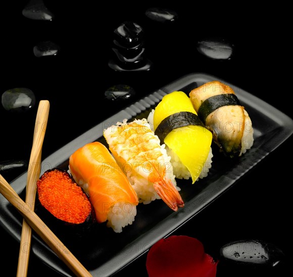 Assorted sushi plate on black pebbles over black background