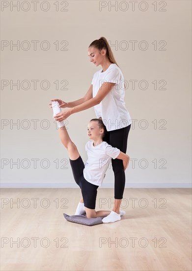 Beautiful female teacher helps a little girl stretch in a gymnastics class. The concept of education