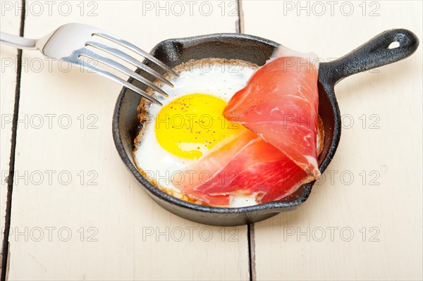 Fried egg sunny side up with Italian tyrolean speck smoked ham on a skillet