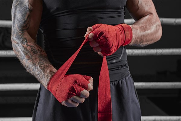 Red bandages on the hands of a kickboxer against the background of the ropes of the ring. The concept of mixed martial arts. MMA