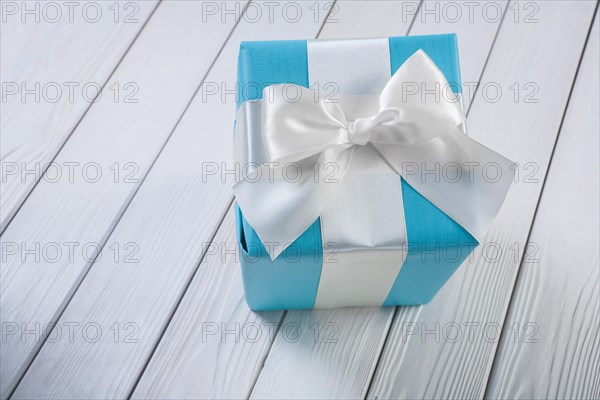 Blue gift box with white ribbon on a white wooden board
