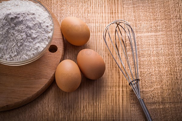 Bowl with flour eggs corolla on wooden board Food and drink concept