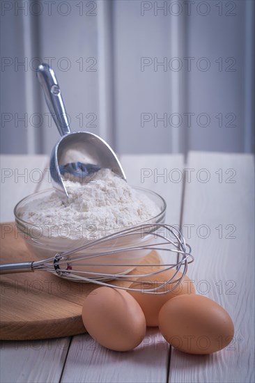 Corola egg bowl with flour scoop on white lacquered old wooden board Food and drink concept