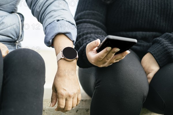 Two beautiful Latina women are proudly displaying their new smartwatch and smartphone. These Hispanic ladies are definitely keeping up with the latest technology trends