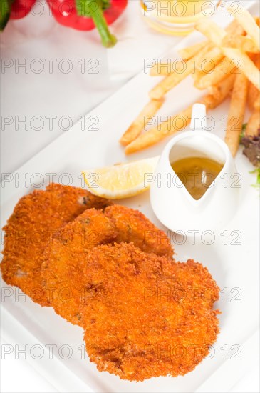 Classic breaded Milanese veal cutlets with french fries and vegetables on background