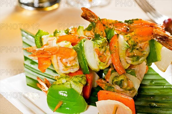 Fresh and colorfull grilled shrimps and vegetables skewers on a palm leaf