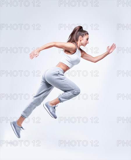 Sports woman runner on a white background. Photo of an attractive woman in fashionable sportswear. Dynamic movement. Side view. Sports and healthy lifestyle. Mixed media