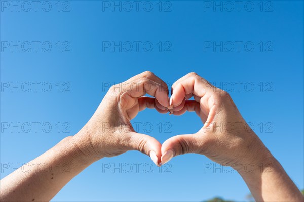 Woman's hands showing heart sign on blue sky background