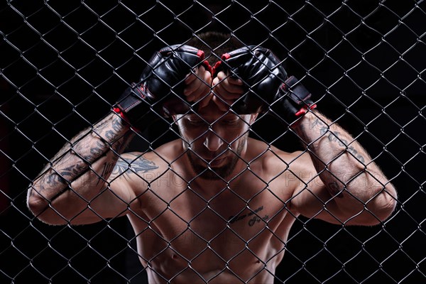 Dramatic image of a mixed martial arts fighter standing in an octagon cage. The concept of sports