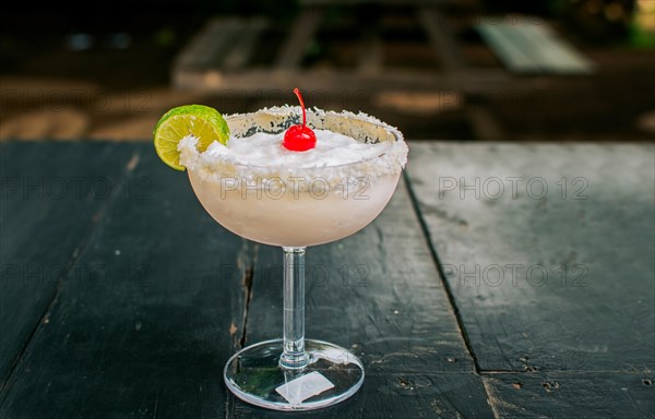 Frozen coconut cocktail with cherry on top on wooden table. Coconut margarita with cherry on wooden table