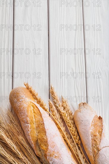 Baguettes and ears of wheat on old white wooden boards with copyspace vertical version