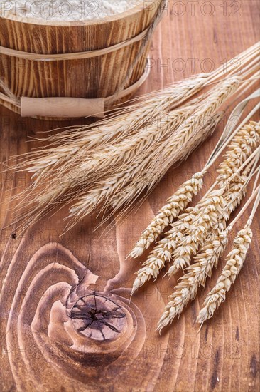 Wheat ears and wooden bucket with flour contept on old board