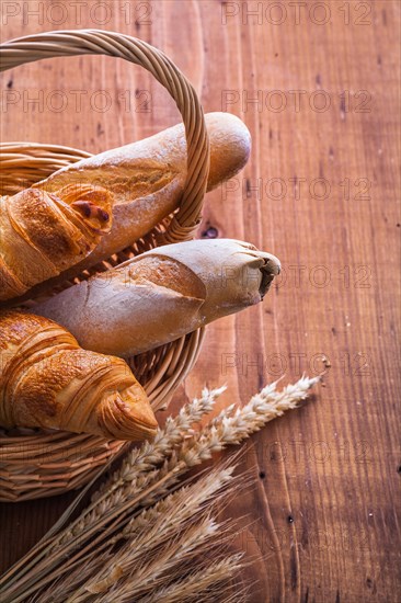 Baguettes and croissants in a wicker basket with ears of wheat