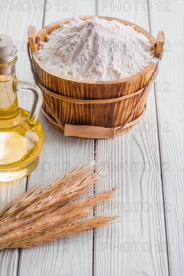 Bucket of flour ears of wheat bottle of oil on old white boards