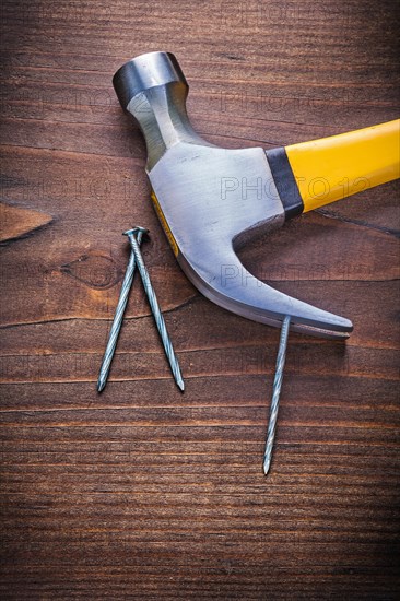 Claw hammer with yellow handle and nails on an old wooden board