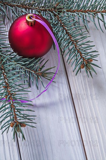 Matt red Christmas bauble and fir tree branch on white wooden panels