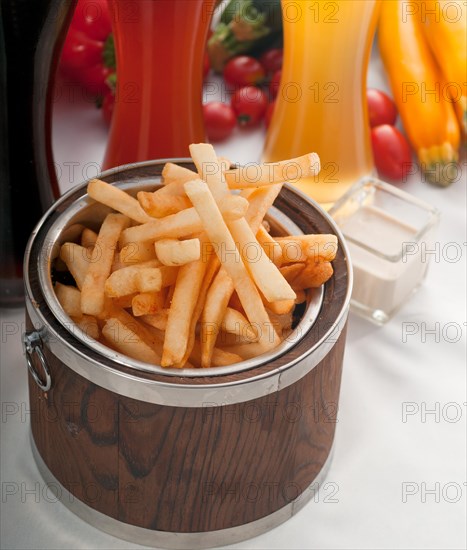 Fresh french fries on a wood bucket with selection of beers and fresh vegetables on background