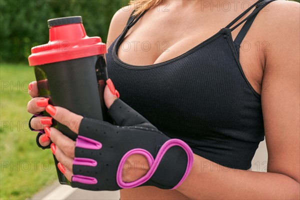 Girl posing with a sports nutrition shaker in the park. The concept of a healthy lifestyle. Sports Equipment. Fitness style advertisement. Mixed media