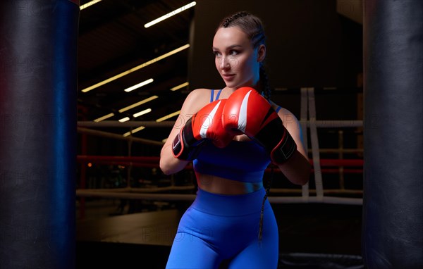 Image of a powerful sportswoman wrestler. Posing in a blue tracksuit and red boxing gloves. The concept of wrestling and boxing. Mixed media