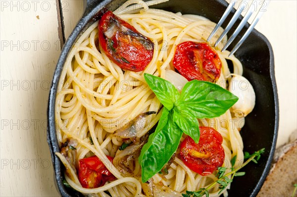 Italian spaghetti pasta with baked tomatoes basil and thyme sauce on a cast iron skillet