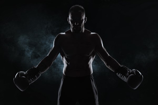 Kickboxer in black gloves posing on a background of smoke. The concept of mixed martial arts. MMA