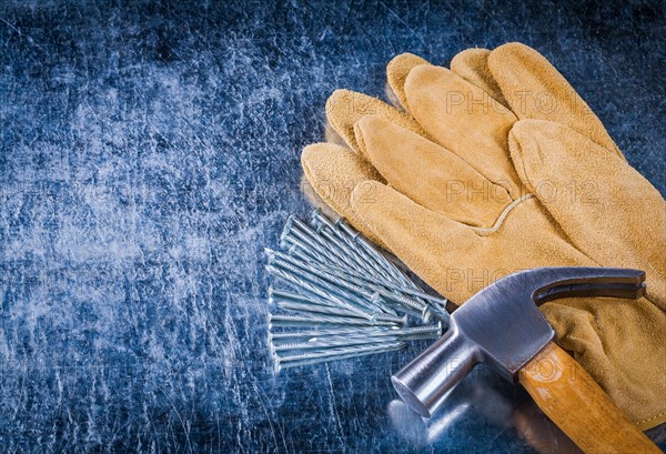 Pair of leather protective gloves construction nails and claw hammer on scratched metallic background copy space image building concept