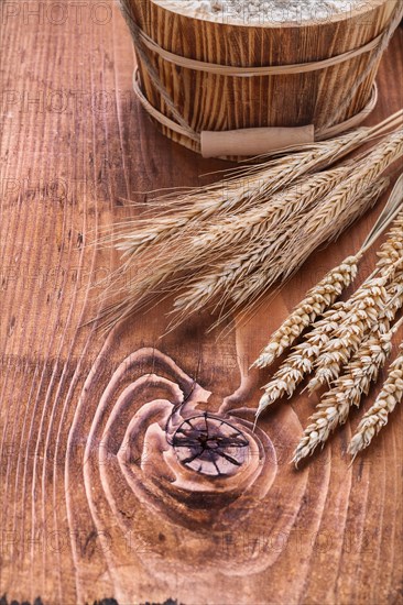 Wheat ears with a bucket of flour on an old wooden board