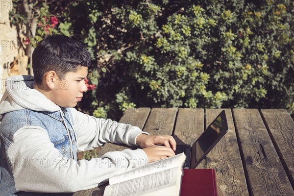 A focused individual works on a laptop at a wooden table outdoors