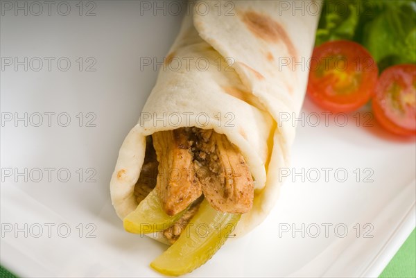 Pita bread chicken roll with pickles cucumbers on a plate with pachino tomatoes and lettuce