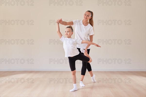 Beautiful woman teacher and a little girl perform dance movements in a bright studio. The concept of education