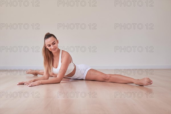 Flexible woman in white sportswear took a splits-legs pose. The concept of gymnastics
