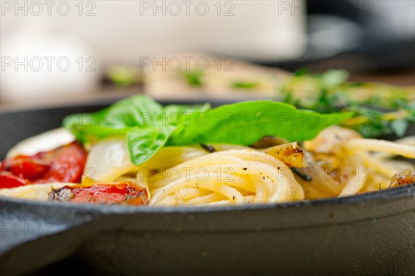 Italian spaghetti pasta with baked tomatoes basil and thyme sauce on a cast iron skillet