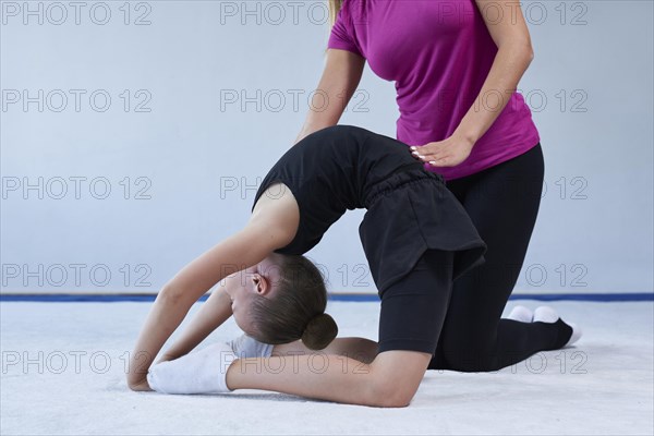 Training in the gym class. A little girl under the guidance of a trainer performs exercises. Gymnastics concept. Mixed media