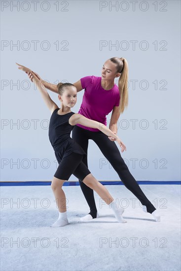 Training in the gym class. A little girl under the guidance of a trainer performs exercises. Gymnastics concept. Mixed media