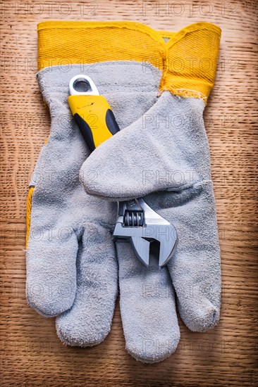 Adjustable spanner and protective work glove on wooden board Construction concept