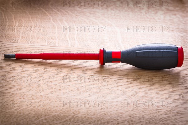 Electrically insulated red screwdriver on wooden board