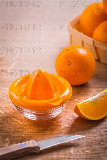 Orange juicer and fruit with kitchen knife on wooden board