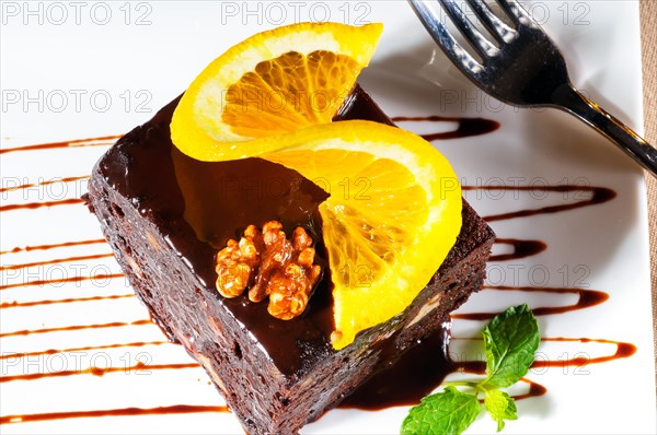 Fresh baked delicious chocolate and walnuts cake with slice of orance on top and mint leaf