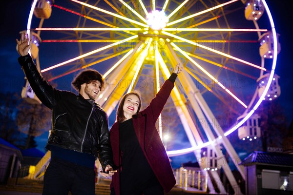 Couple in love in an amusement park near a ferris wheel on a date in cold weather. The concept of love and joy in relationships