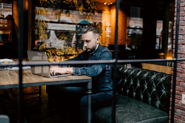 Young successful focused freelancer in a denim shirt working enthusiastically at a laptop in a covoking space