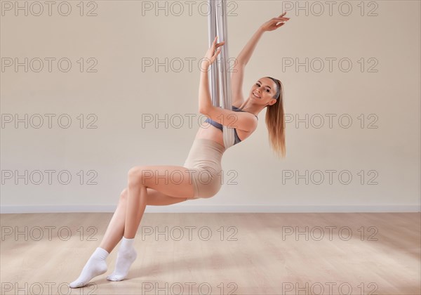 Image of a beautiful woman posing in a bright studio near the hammocks. The concept of airstretching. Fitness and sports