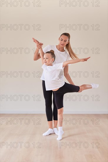 Beautiful woman teacher and a little girl perform dance movements in a bright studio. The concept of education