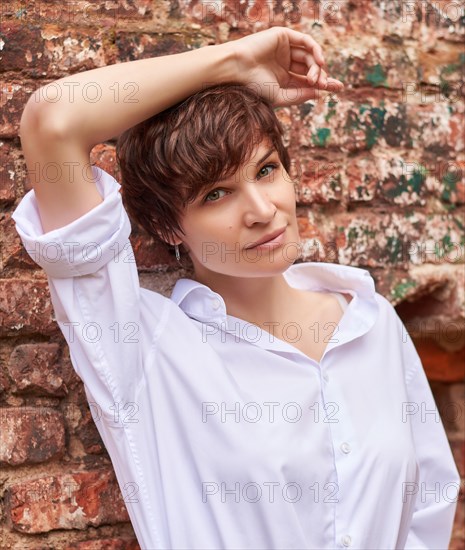 Retro portrait of a stylish beautiful woman in a white shirt against the background of a destroyed building. The concept of style and fashion