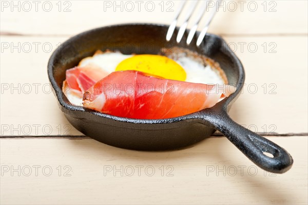 Fried egg sunny side up with Italian tyrolean speck smoked ham on a skillet