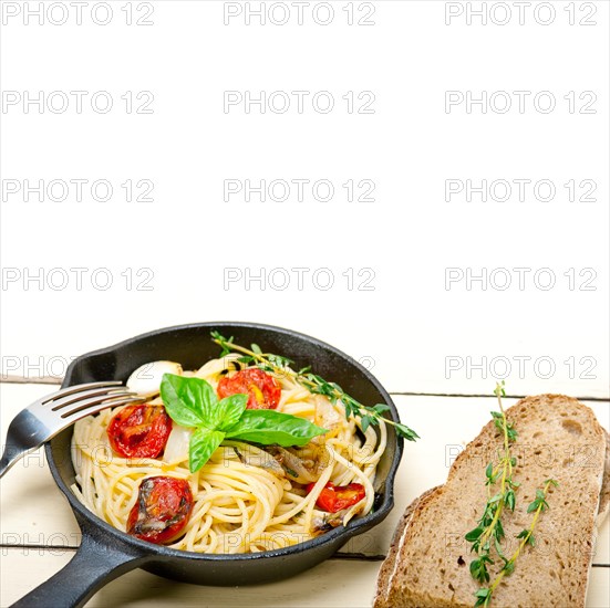 Italian spaghetti pasta with baked tomatoes basil and thyme sauce on a cast iron skillet