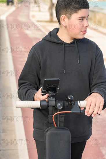 Young teenager with a sideways glance riding an electric sscooter and using a smartphone application E-Mobility urban leisure concept